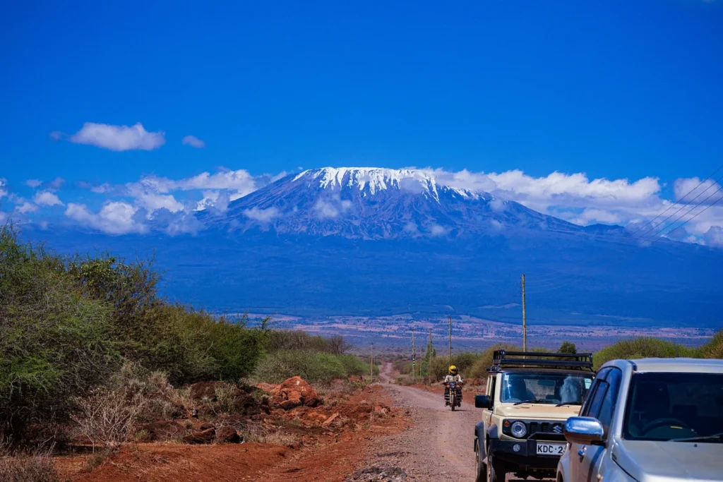 Mount Kilimanjaro rising above a road and safari vehicles